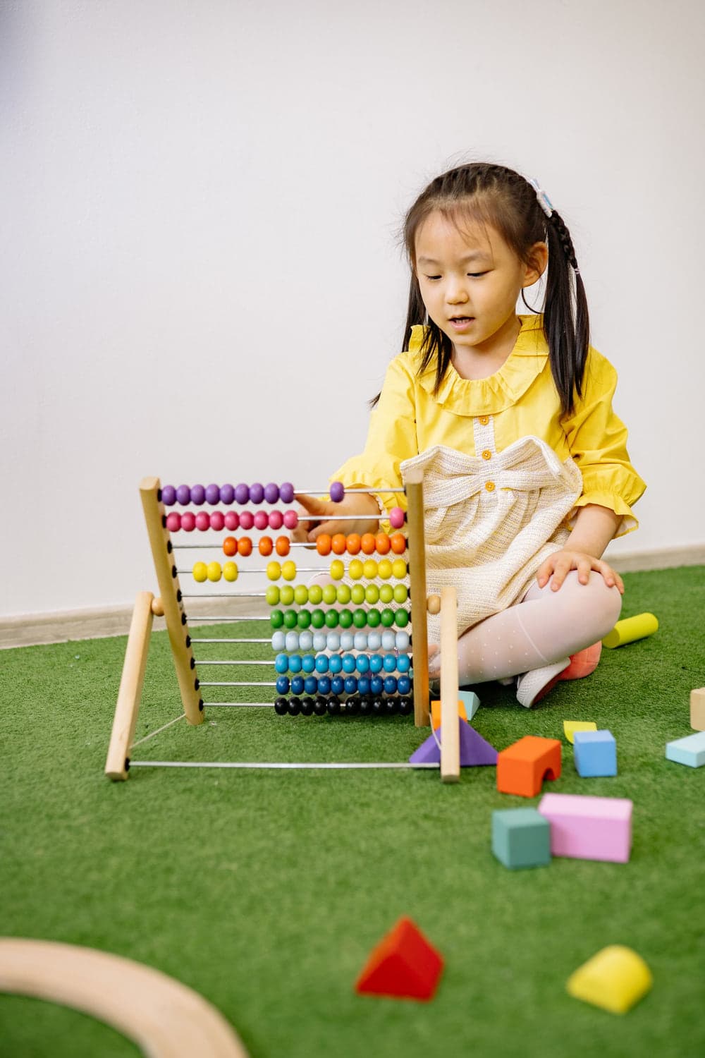 A young child counting beads on a wooden abacus