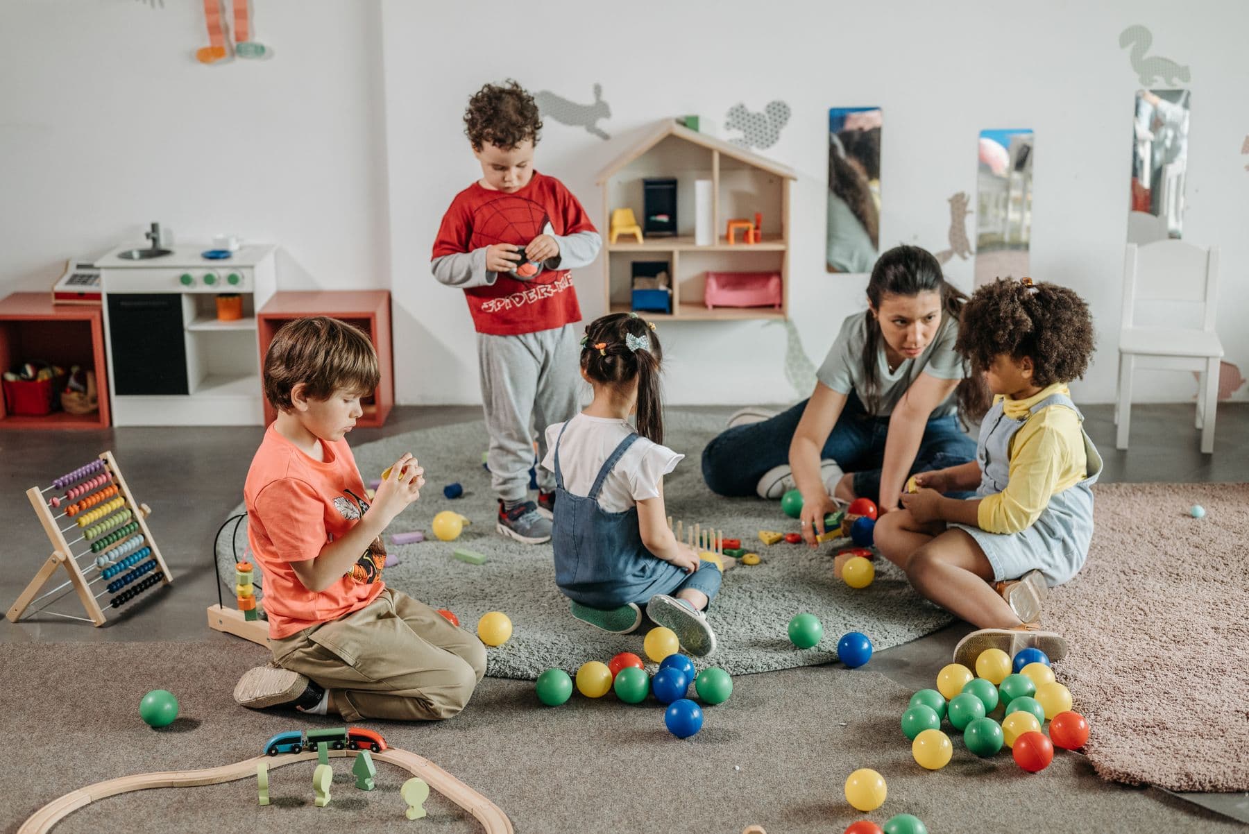 A teacher sitting on the floor with four young children and wooden toys