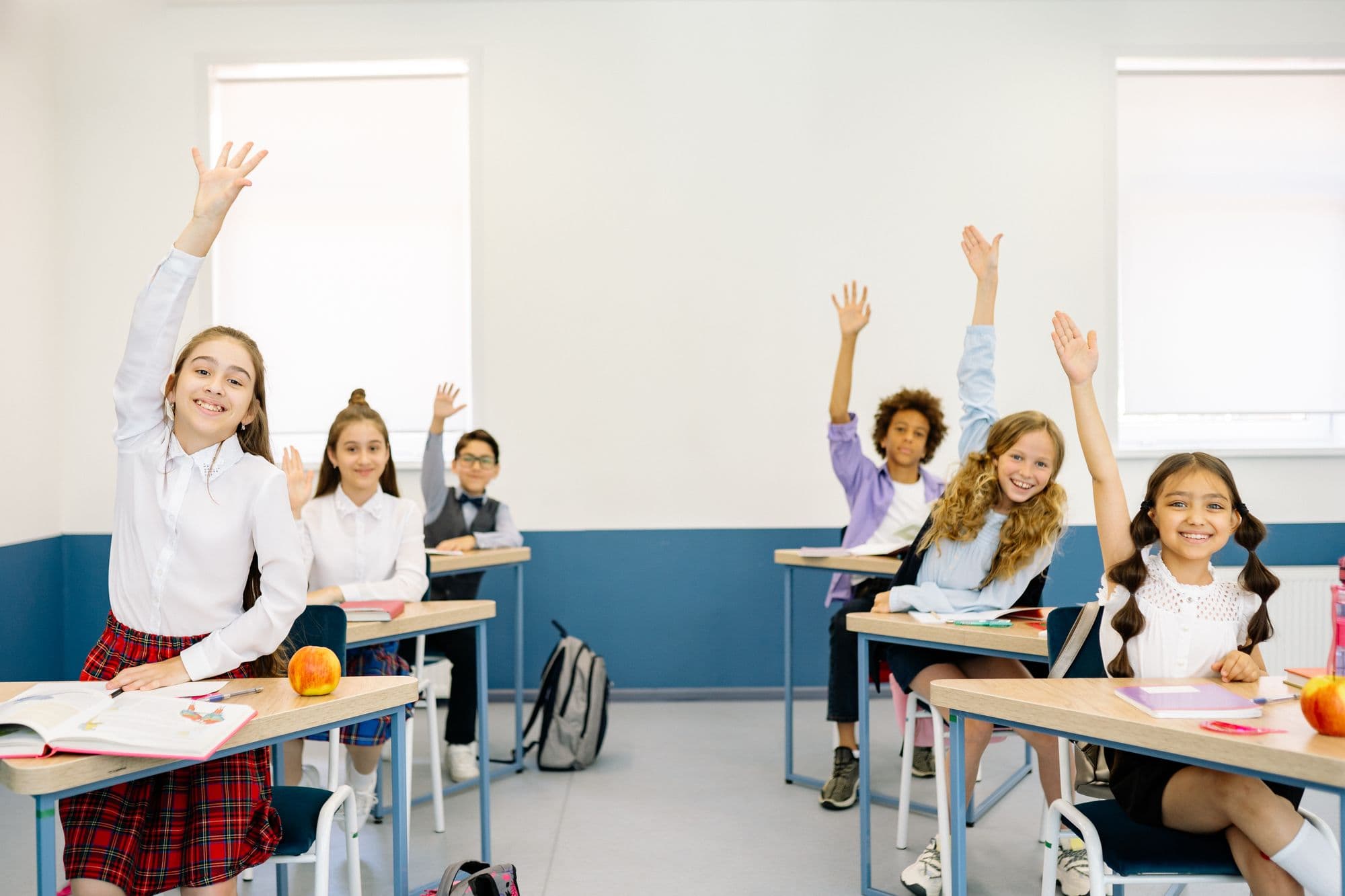 Primary-age children at their desks with hands raised during a classroom lesson