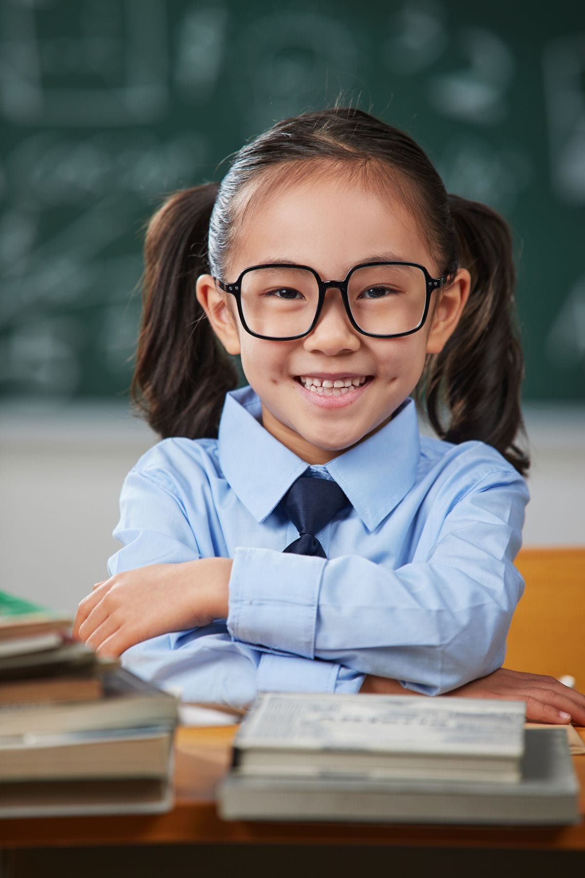 A young primary student in school uniform smiling at her desk with her books